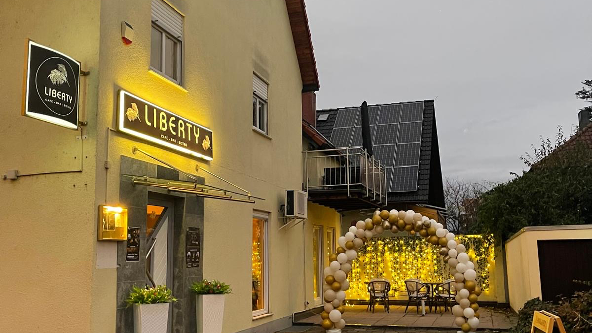 Beleuchtete Außenfassade des Liberty Café Bistro in Schwaikheim am Abend mit Leuchtschild und Ballonbogen